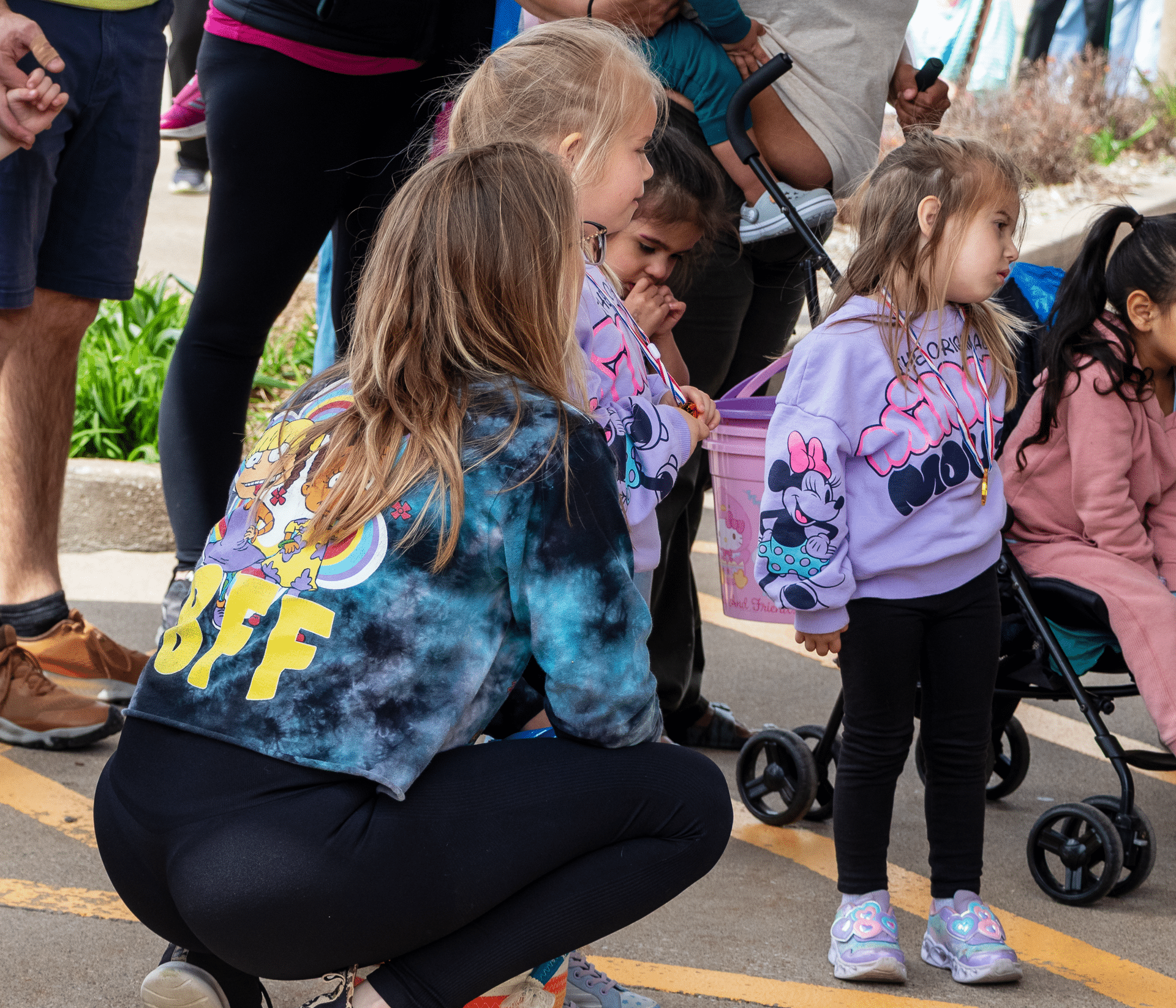 Three smiling girls gather outdoors, surrounded by caring adults and kids—sharing joy in our church family. - Muscatine Church of Christ