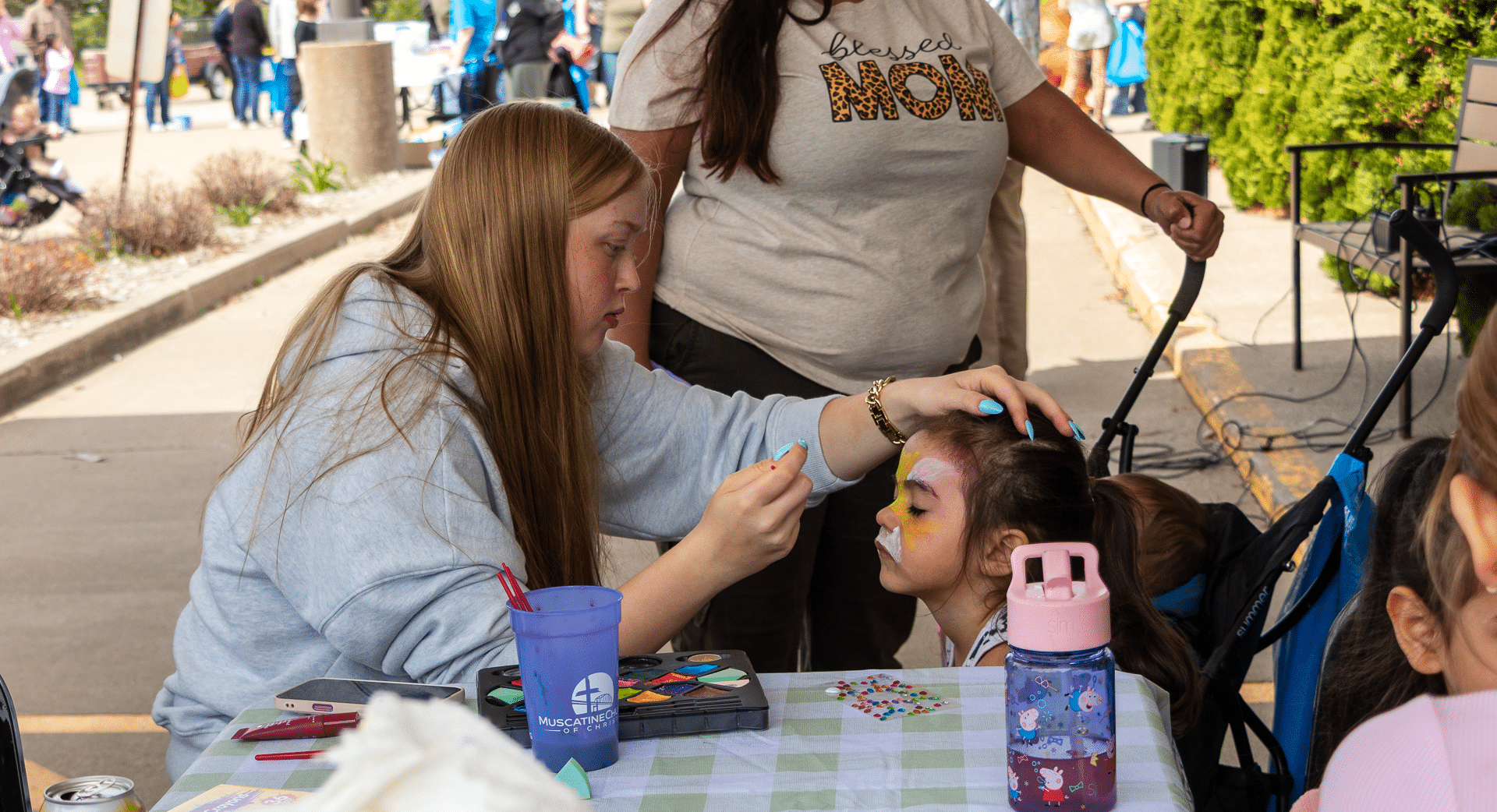 A joyful moment as a woman paints a butterfly on a girl’s face—celebrating community, welcome, and hope together. - Muscatine Church of Christ