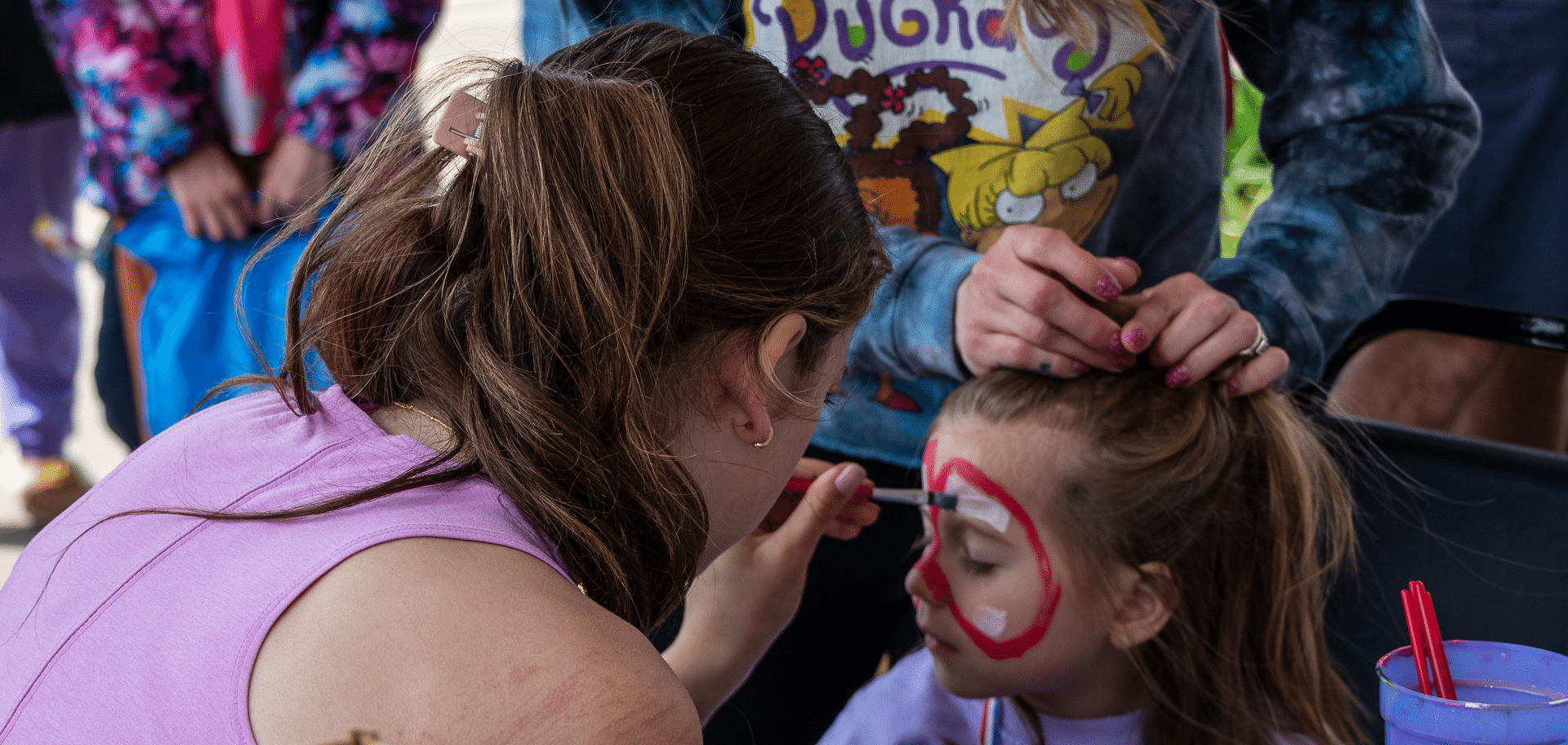 A caring volunteer paints a child’s face as others help—sharing fun, friendship, and hope in our church family. - Muscatine Church of Christ