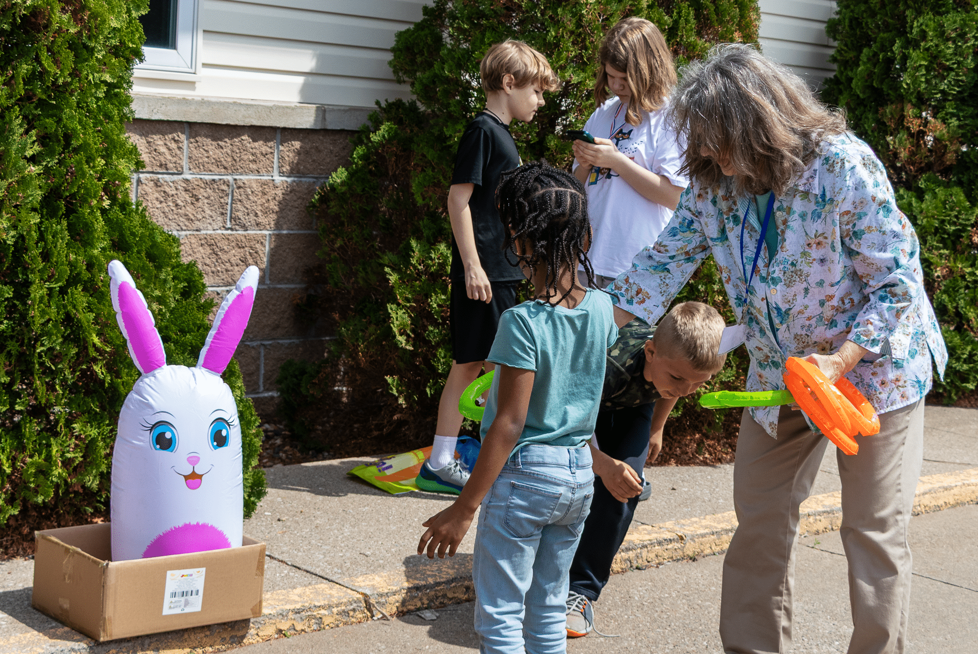 Children and an adult share smiles and laughter playing ring toss together outside—everyone welcome in our church family. - Muscatine Church of Christ