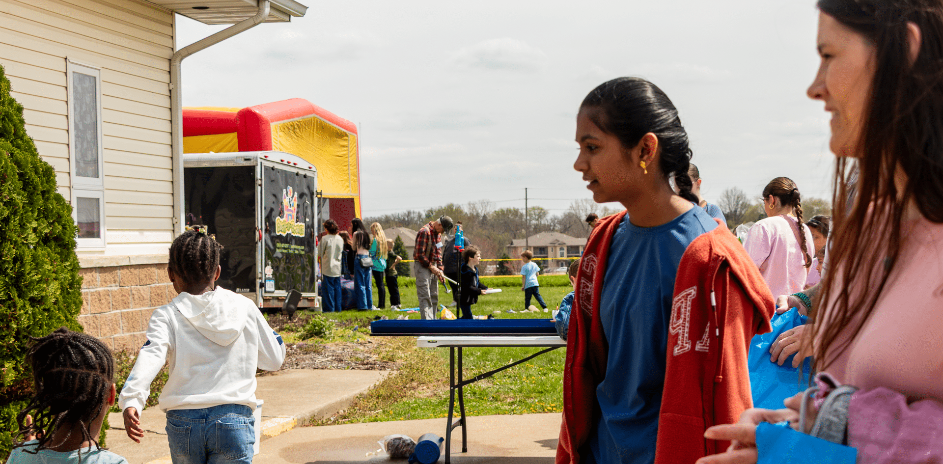 Friends and families gather outside, sharing smiles and hope beside a bounce house at our welcoming church event. - Muscatine Church of Christ