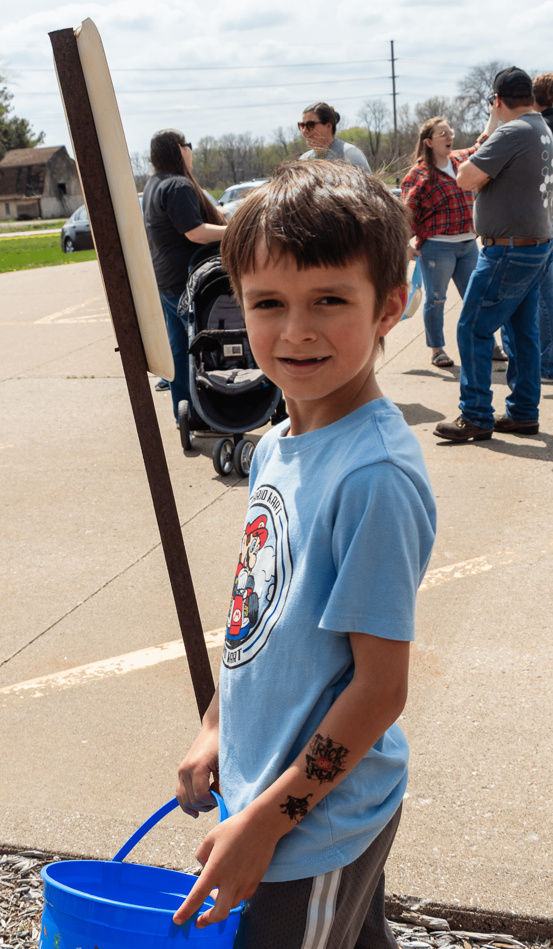 Smiling boy with blue bucket welcomes you; friends connect in the sunshine behind him. All are invited to belong here. - Muscatine Church of Christ