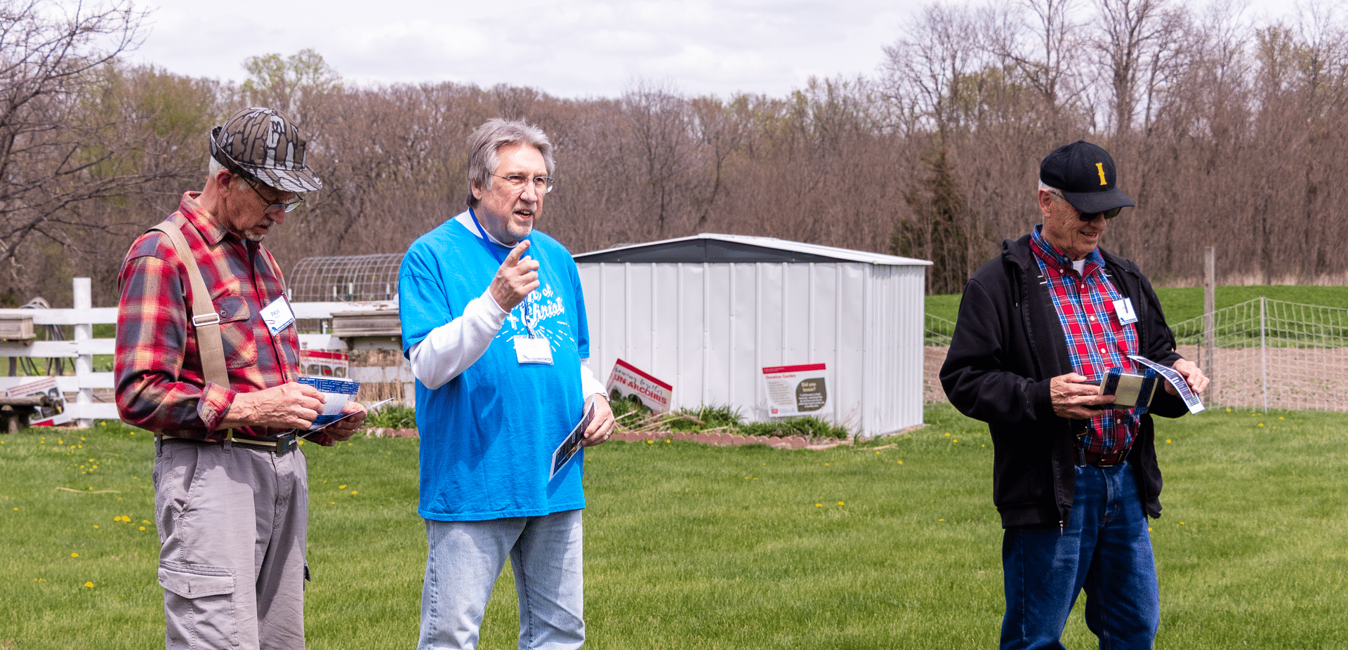 Three men gather outside with booklets, sharing smiles and hope—welcome to our church family community. - Muscatine Church of Christ