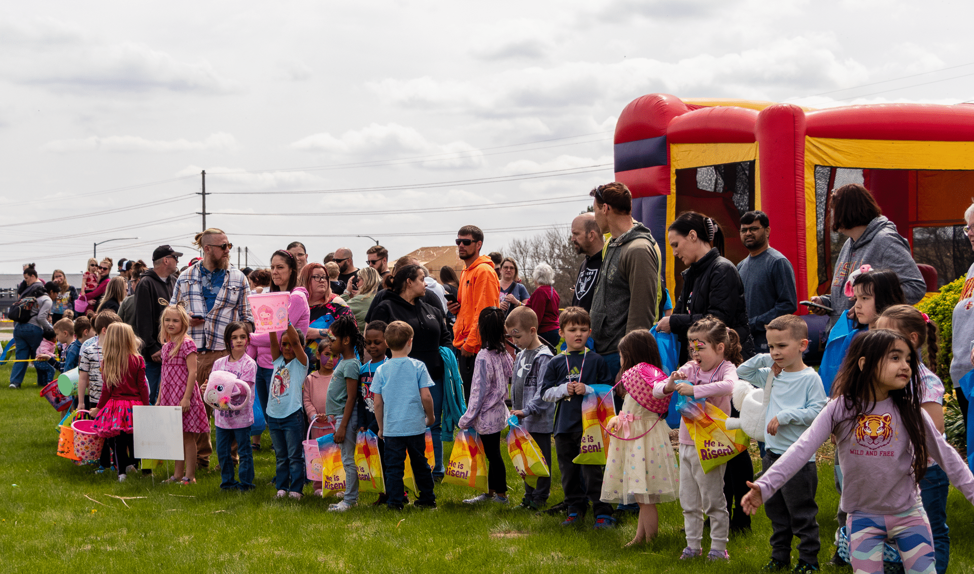 Families and children gather with bags and smiles by a bright bounce house, enjoying joyful moments together. - Muscatine Church of Christ