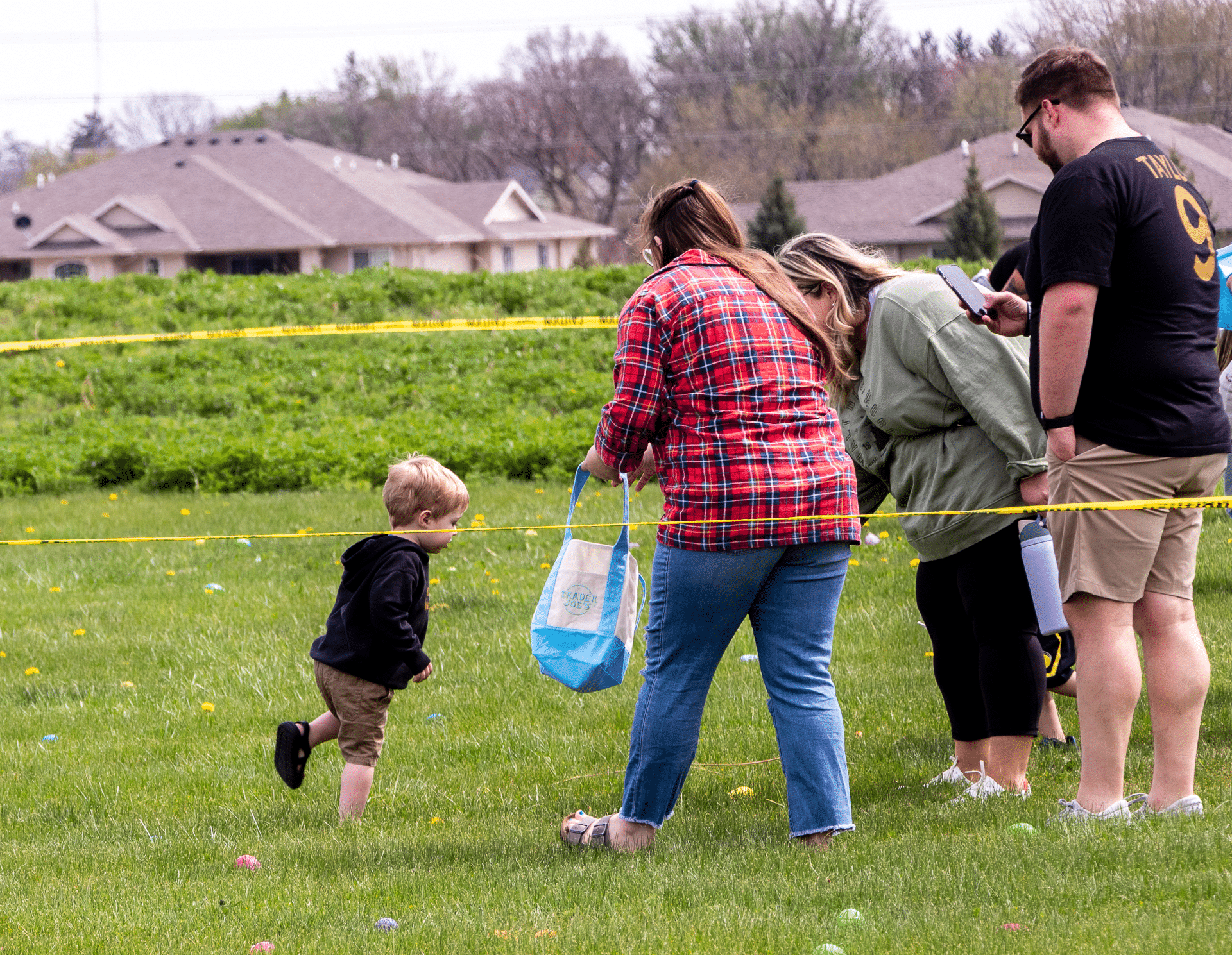 A child joyfully greets a welcoming woman with a blue bag as neighbors gather in fellowship on the sunny green lawn. - Muscatine Church of Christ