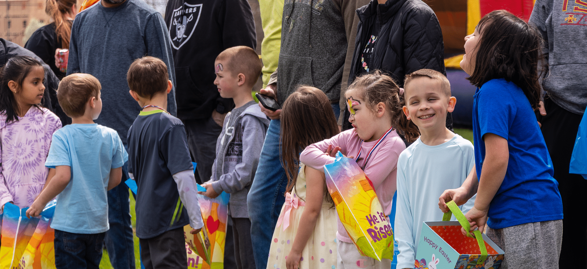 Smiling children with colorful bags and books, surrounded by caring adults—everyone welcome in our hopeful community. - Muscatine Church of Christ