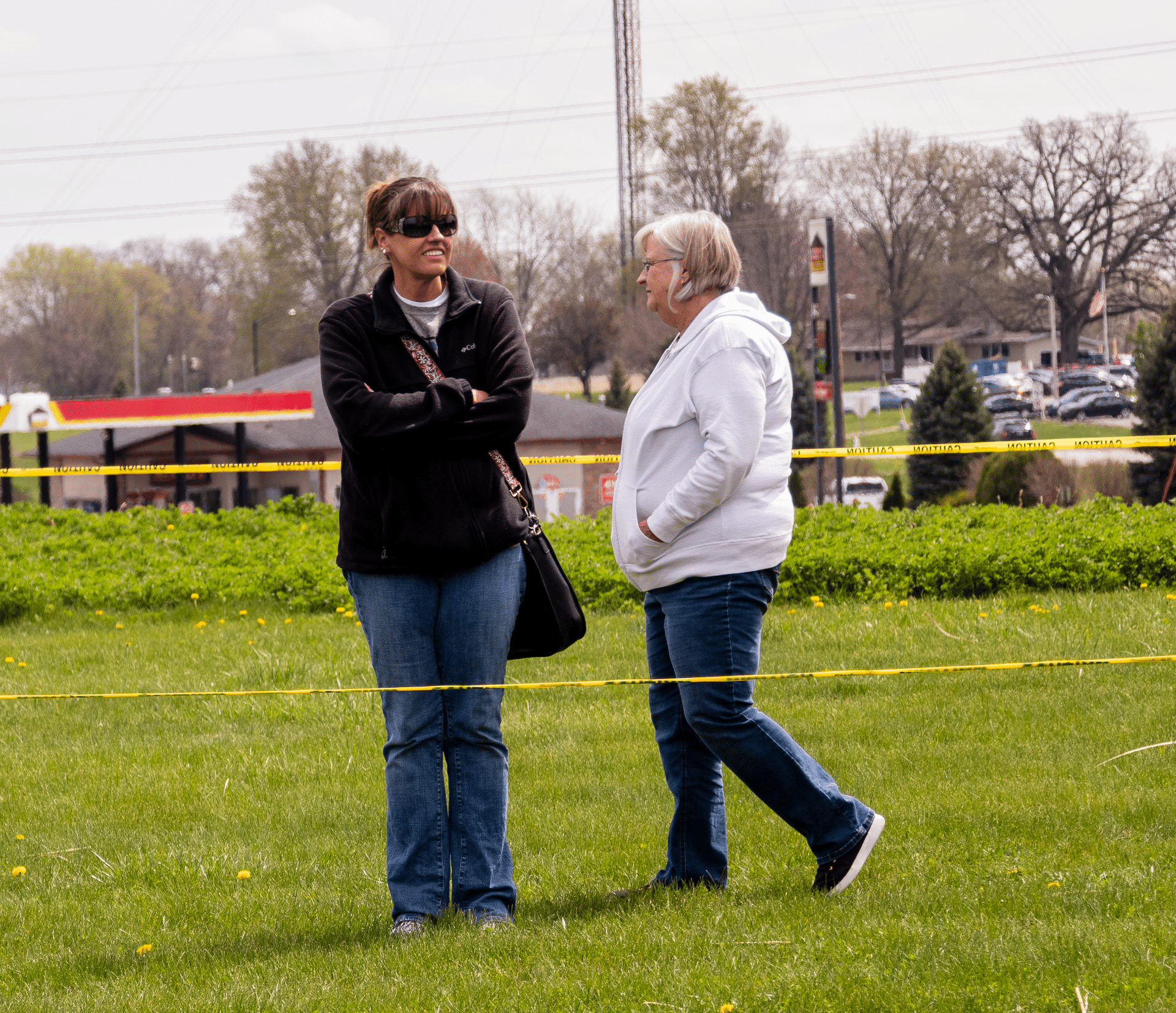Two women share a warm conversation outdoors, surrounded by trees and buildings—welcome and hope in our community. - Muscatine Church of Christ