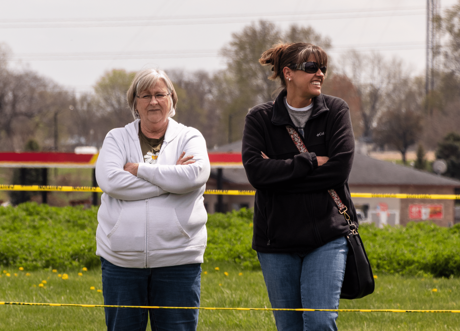 Two women smile together on the grass, ready to welcome all into our church family and community of hope. - Muscatine Church of Christ
