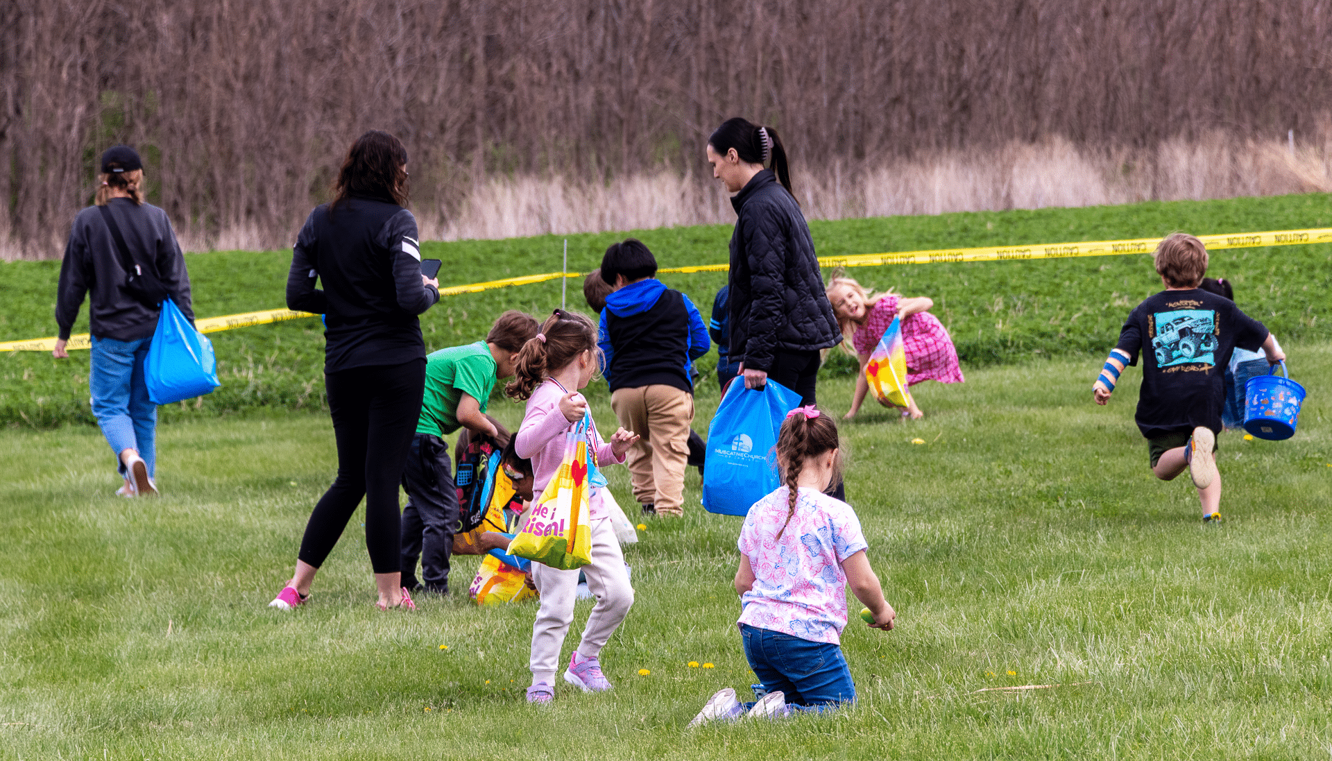 Families and children joyfully hunt for eggs together on a sunny lawn, sharing laughter, hope, and community. - Muscatine Church of Christ