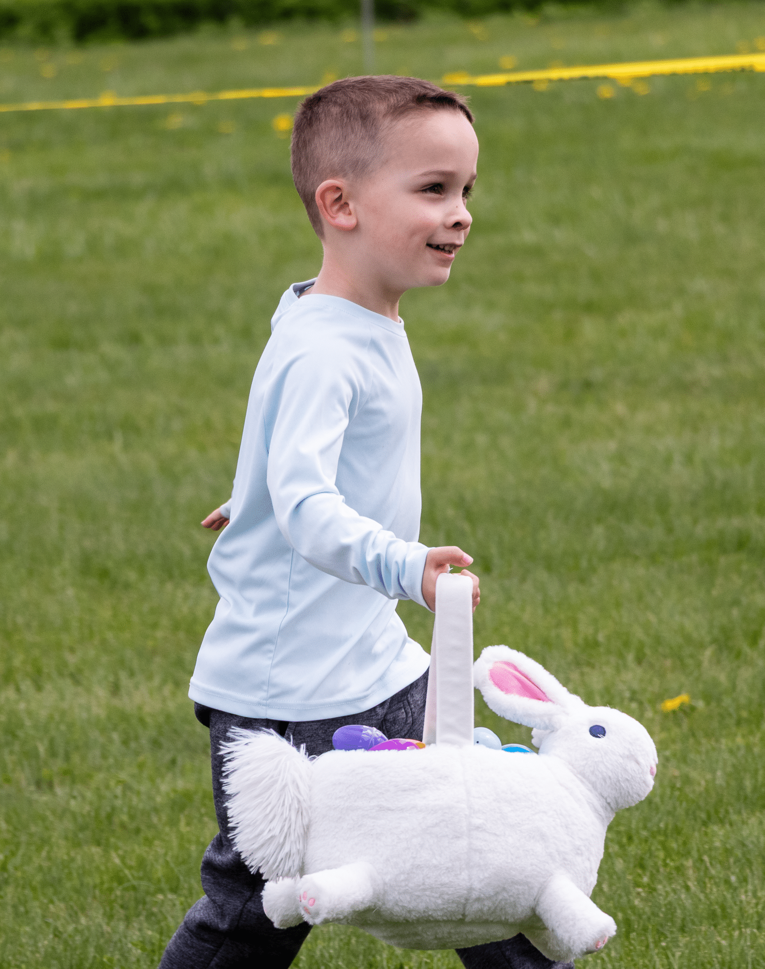 A smiling child carries a bunny basket of colorful eggs, sharing joy and hope in our church community garden. - Muscatine Church of Christ