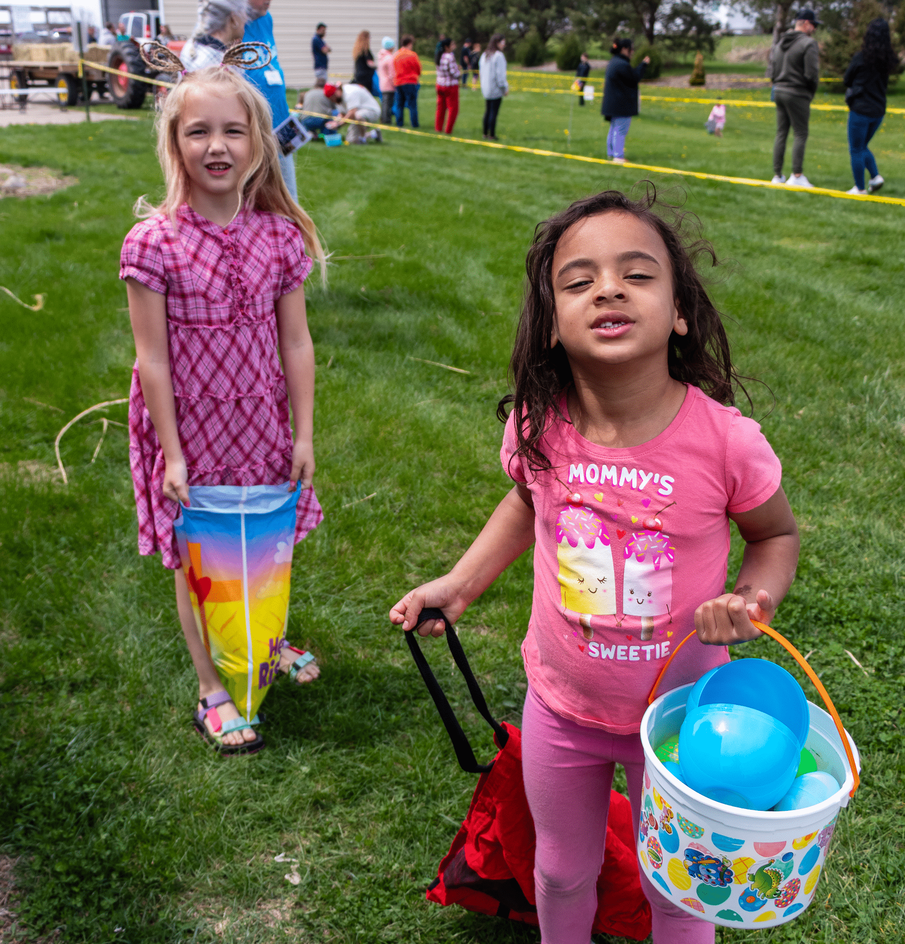 Two smiling girls with bright buckets enjoy a joyful outdoor gathering, surrounded by our welcoming church family. - Muscatine Church of Christ