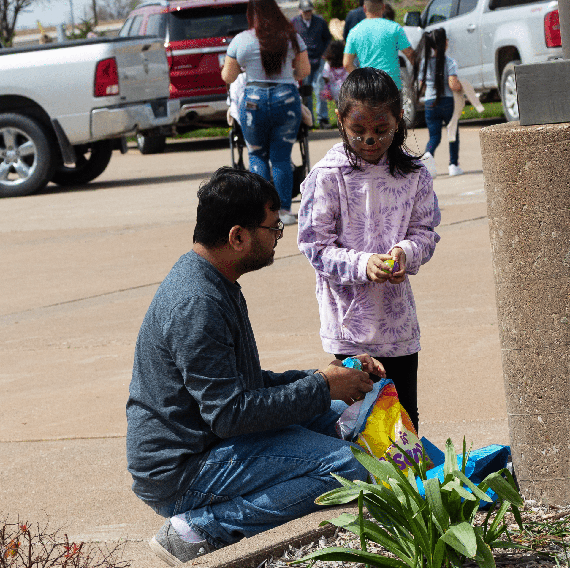 A caring adult kneels beside a joyful, face-painted child outdoors—sharing moments of hope, joy, and community together. - Muscatine Church of Christ