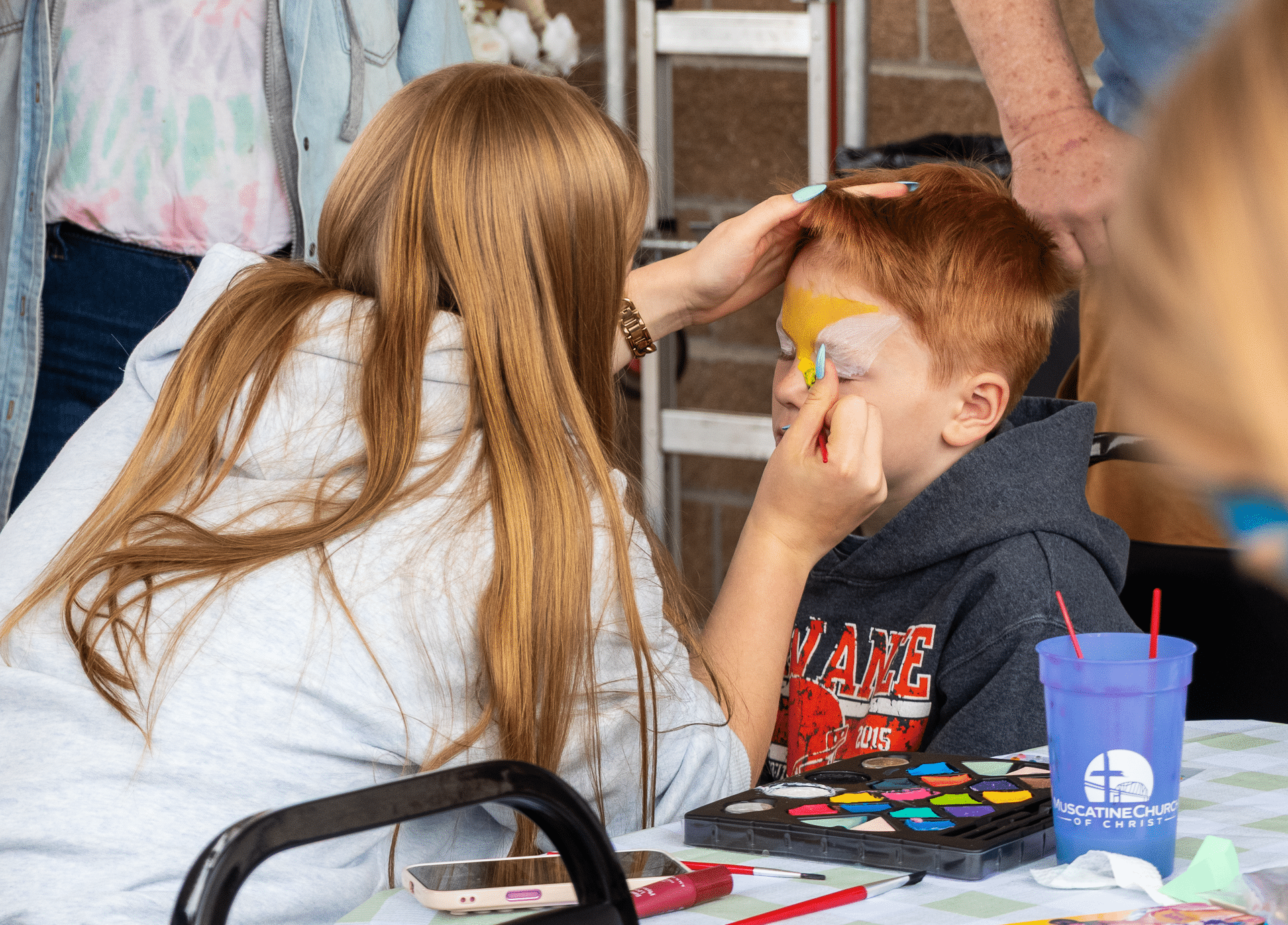 A welcoming moment: a woman paints a boy’s face with joy, sharing smiles and hope in our church community. - Muscatine Church of Christ