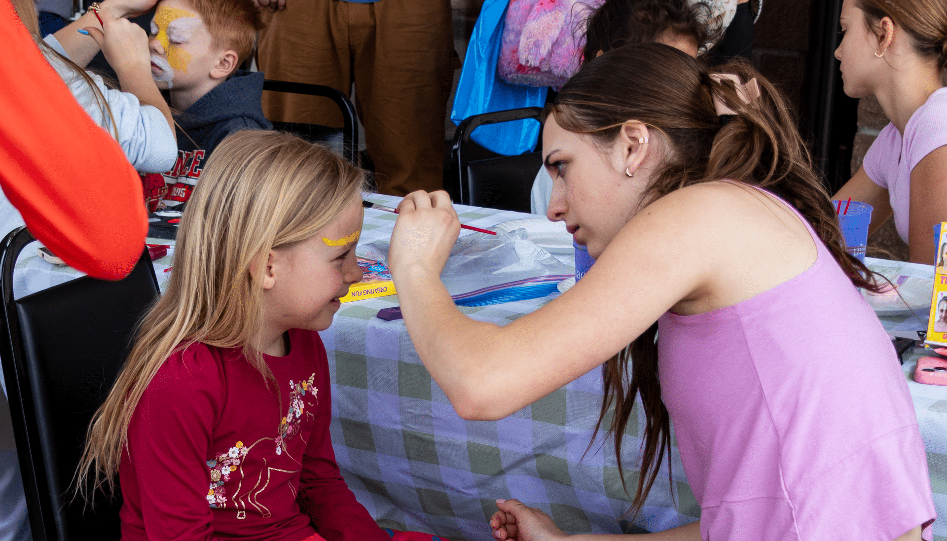 A welcoming community gathers indoors as a smiling girl gets her face painted, sharing joy and hope together. - Muscatine Church of Christ