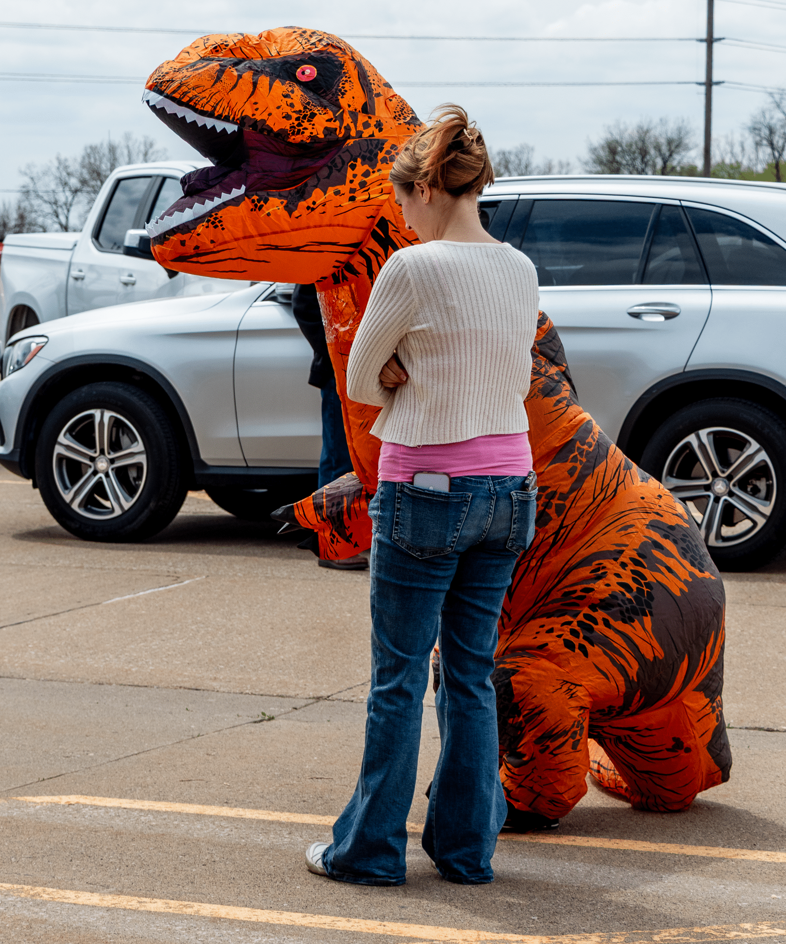 Two friends, one in a cozy sweater and one in a fun dino suit, share smiles together in our parking lot. - Muscatine Church of Christ