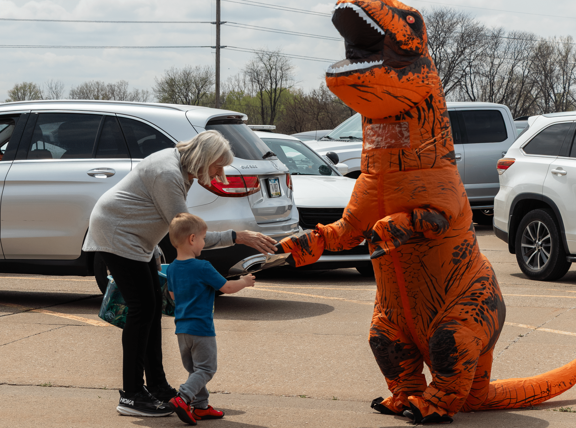 A friendly dino greets a smiling boy and his grandma in our parking lot—sharing joy, hope, and community together. - Muscatine Church of Christ