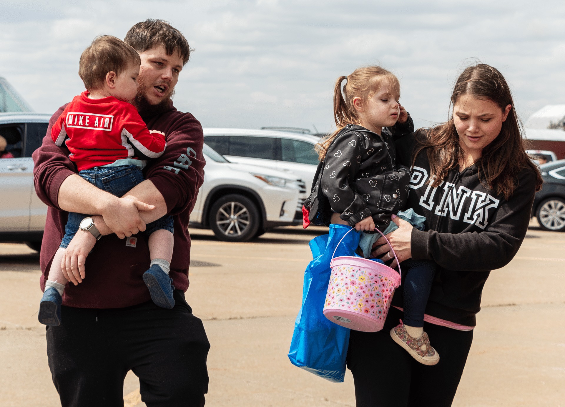 A joyful family carries children and Easter gifts, sharing hope and welcome in our church community parking lot. - Muscatine Church of Christ